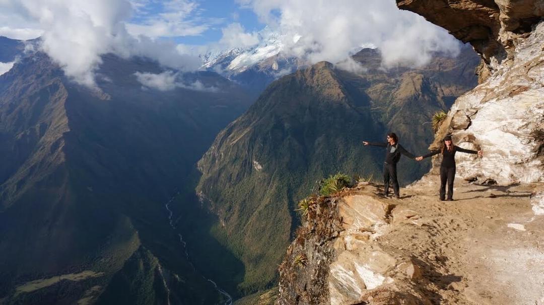 Two people standing on a cliff edge in front of a mountain view